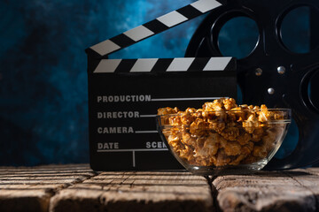 Popcorn film reel and movie clapper on wood background. Screensaver for the inscription of the rest...