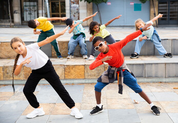 International group of modern tweenagers performing street dance choreography outdoors in summer.
