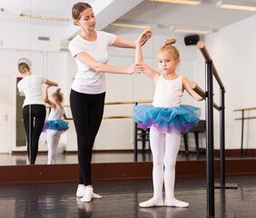 Little ballerina practicing choreographic elements with help of ballet teacher in dance hall