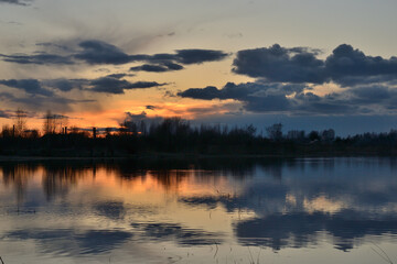 Spring landscape with dramatic after-sunset sky reflected in the water, silhouettes of trees on the shore. Evening calm on the river. Bright afterglow.