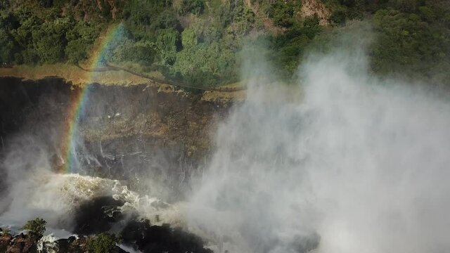 The Victoria Falls at the Border of Zimbabwe and Zambia in Africa. The Great Victoria Falls One of the Most Beautiful Wonders of the World. Aerial Shot. Rainbow in the Background. Camera Moves Upward