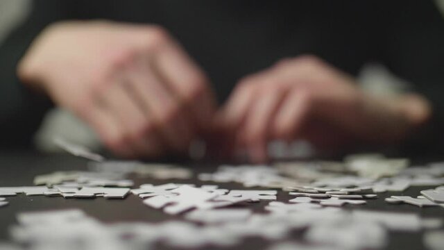 Puzzle pices falling on a dark table and bouncing off with a person's hands trying to solve the puzzle in the background. Shot in 4K, Slow Motion with Shallow Depth of Field.	