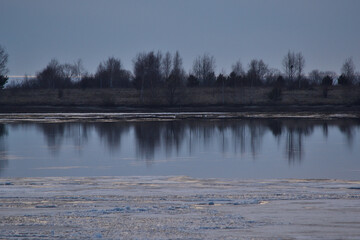 A landscape view of the frozen sea during ice drift in spring with dramatic sky and with reflections in melt water in the evening at sunset. In the distance, the black strip of the island.