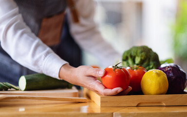 A female chef holding and picking a fresh tomato from a vegetables tray on the table