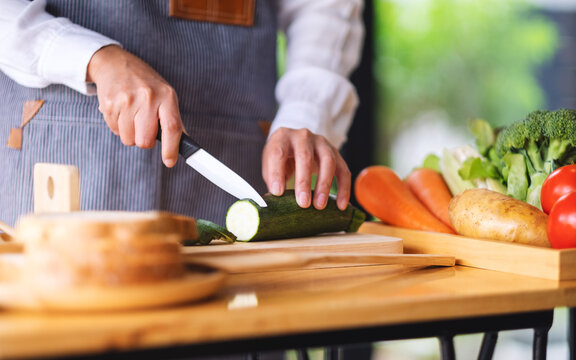Closeup image of a female chef cutting and chopping vegetables by knife on wooden board in kitchen