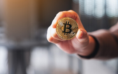Closeup image of a hand holding and showing a gold colour bitcoin