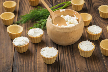 Wooden bowl with cream cheese and tartlets on a wooden table.