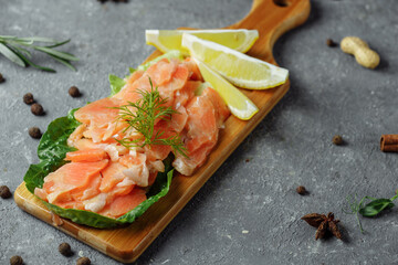 Pieces of fried salmon with dill and lemon wedges on a wooden board