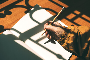 Elder hand hold pencil writing with sun light and shadow on wood table.