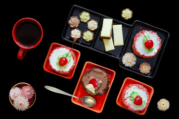Cherry cakes, candies and a cup of coffee on a black background. Top view