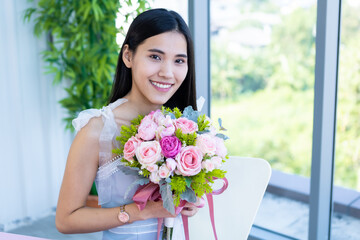 Valentine's day concept, Happy of smiling Asian young female sitting at a table food holding a bouquet of roses at in the restaurant background