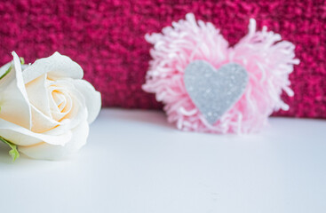 A white rose bud with a close-up of the edge against the background of a pink heart-shaped pompom 