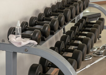 Cleaning exercise machines with alcohol sanitizer spray before lifting dumbbells in the gym or fitness. prevent Coronavirus infection,safety of the COVID-19 outbreak. Selective focus.