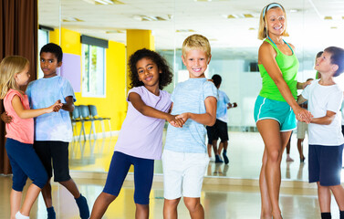 Group of preteen children training movements of slow foxtrot in dance studio with female...