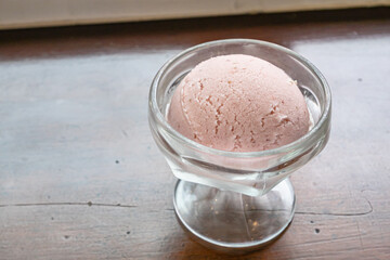 The close up of tasty homemade cool strawberry ice cream scoop in glass cup on vintage wood table background.