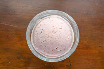The close up of tasty homemade cool strawberry ice cream scoop in glass cup on vintage wood table background.