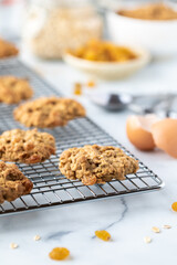 Close up of oatmeal raisin cookies on a metal cooling rack with recipe ingredients in soft focus in behind.
