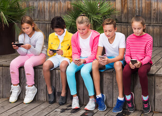 Cheerful children are playing on smartphone in the playground