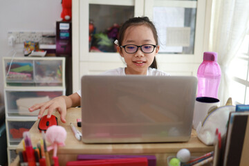 Cheerful young little Asian girl teenage using laptop computer at home during the pandemic lockdown, Homeschooling and online e-learning at home concept.