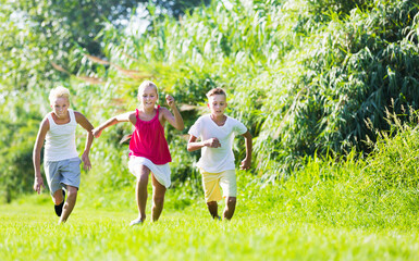 Fototapeta premium Smiling adult kids playing active games in summer park chasing each other