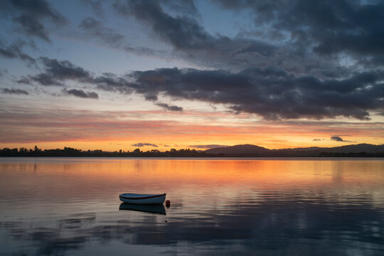 Small dinghy in bay with reflected orange golden hour light in Tauranga New Zealand.