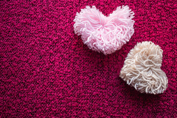 Two fluffy pompoms made of pink and beige heart-shaped ponies on a crimson background 