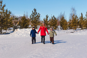 happy young mother and two children run holding hands in the park. people in winter