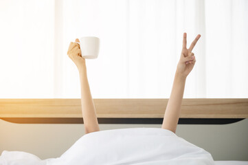 Woman waking up in the morning on bed. She hiding under the blanket and stretching out two arms...