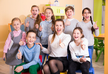 Cheerful group of pupils with female teacher posing together in schoolroom, giving thumbs up