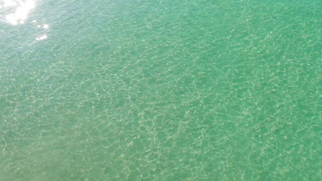 Crystal clear cyan blue sea water surface n calm ocean wave or ripple with bright shining sun glare n sunlight ray flare in tropical summer or spring sunshine day, 4k cinemagraphs b-roll footage video
