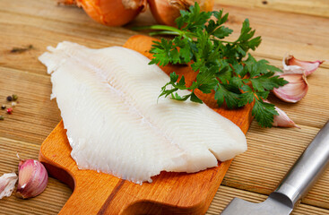 Fresh raw halibut fillet with greens and spices on wooden background. Cooking ingredients