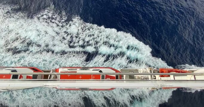 orange lifeboats on Portside of a cruise ship on a voyage with waves rooling back to the sea with a mirror view. Atop wide steady shot 