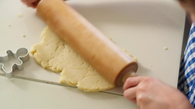 boy rolls out cookie dough with rolling pin Close-up hands boy rolling out shortbread dough into thin pancake, cutting out cookie figures from dough using cookie cutters. 4K Video