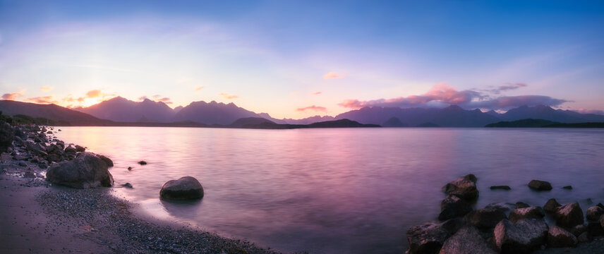 Colorful sunset panorama at Lake Te Anau - Patience Bay - with reflections in the water and mountain range silhouetted in the background in Fiordland National Park, New Zealand, South Island.