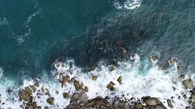 Aerial view of big waves break on rocks in a blue ocean with Sea waves on beautiful tropical sea Drone camera 4k shot Bird's eye view of ocean waves crashing against empty stone rock cliff from above