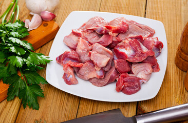 Fresh clean raw chicken gizzards in white plate with seasonings on wooden background