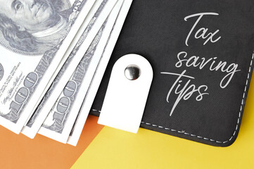 Top view of money banknotes, notebook written with text TAX SAVING TIPS over yellow and orange background. 