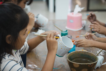 Asian child girl and friends are concentrating to paint on ceramic glass with oil color together...