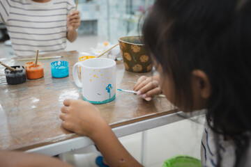 Asian child girl and friends are concentrating to paint on ceramic glass with oil color together with fun. Kids arts and crafts creative activity class in school.