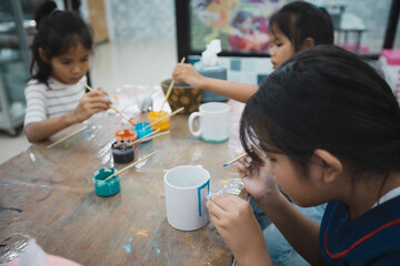 Asian child girl and friends are concentrating to paint on ceramic glass with oil color together with fun. Kids arts and crafts creative activity class in school.