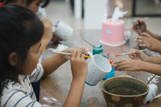 Asian child girl and friends are concentrating to paint on ceramic glass with oil color together with fun. Kids arts and crafts creative activity class in school.