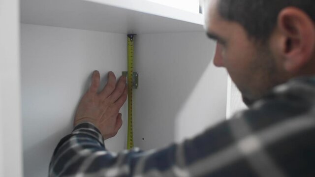 Carpenter measuring shelves that are parts of new kitchen with meter.