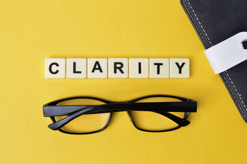 Selective focus with noise effect of notebook, eyeglasses and scrabble alphabets with text CLARITY over yellow background
