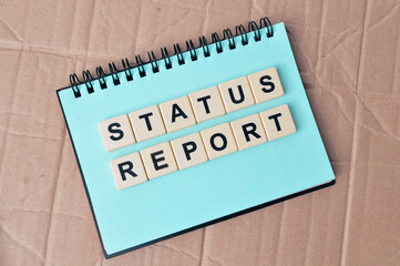 Top view of notebook and scrabble letters with text STATUS REPORT over cork board background. Business concept
