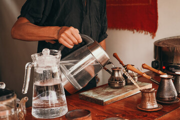 A woman pours boiling water into a cup. The barista prepares coffee on the sand. Traditional coffee preparation