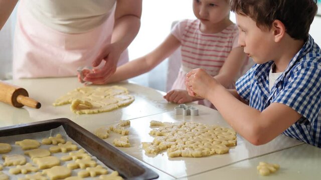 Children and mother bake cookies. close-up with their hands, a boy and a girl cut cookie molds out of the dough using cookie cutters and put them on a baking sheet in the kitchen. 4K Video