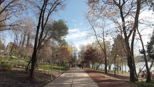 Walkway leisure path crossing Tirana's Grand park alongside the artificial Lake in Albania - Wide push in dolly shot 