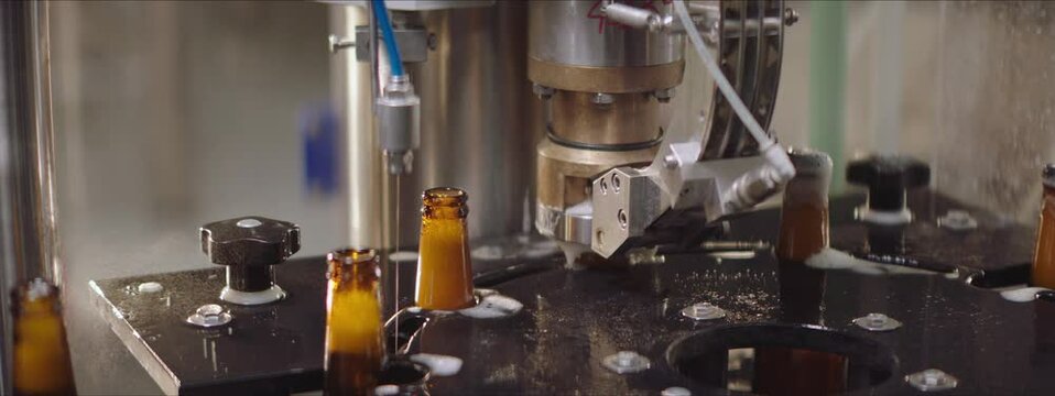 Glass beer bottles moving on a modern machinery. Capping process of full beer bottles. Foam overflowing the bottles. Factory, brewery concept.