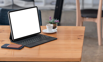Mockup blank screen tablet with magic keyboard on wooden table in cafe.