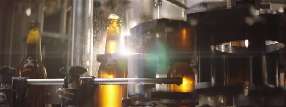Close-up video of a beer manufacturing process. Full beer bottles moving on a modern industrial machine. Factory, brewery concept.